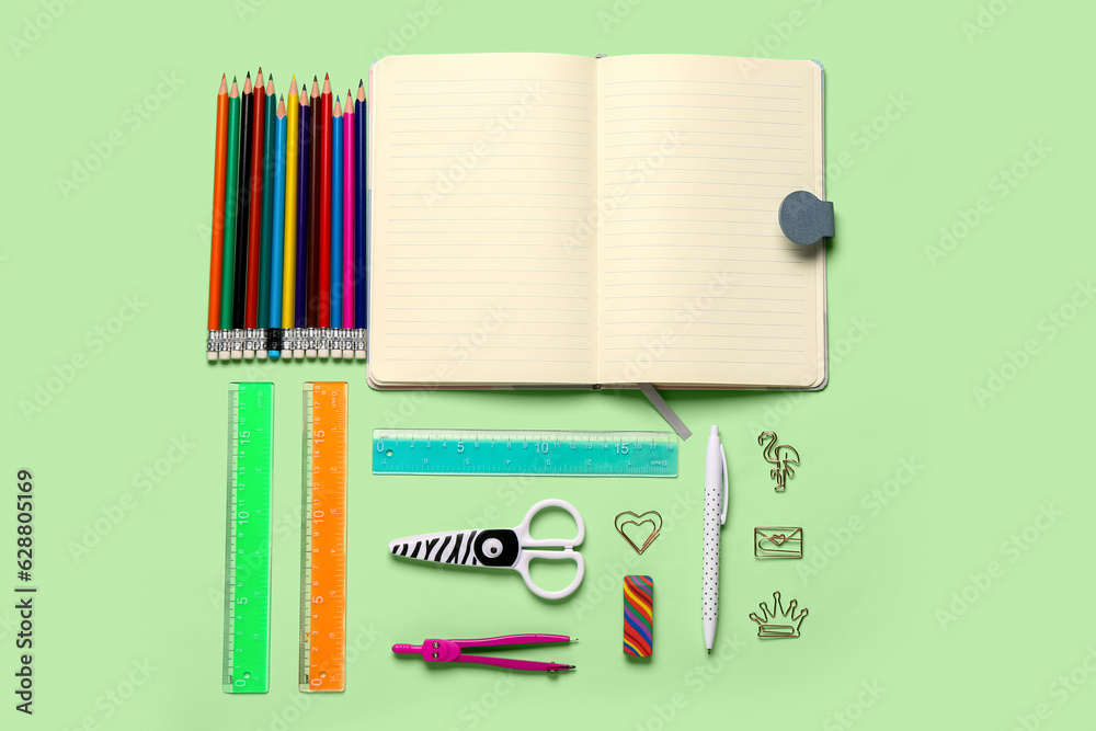 Notebook with different stationery supplies on green background