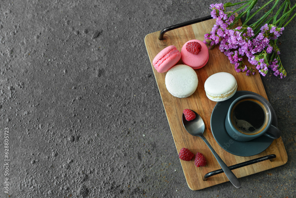 Wooden tray with sweet macaroons and cup of coffee on dark background