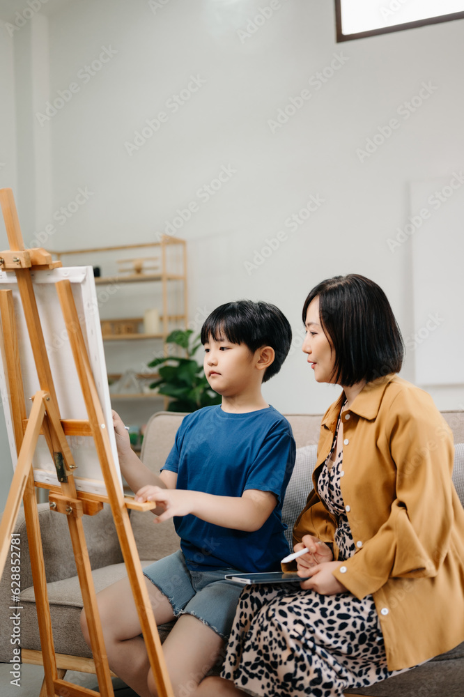 Asian Woman assisting young boy in painting on canvas. Happy woman looking at her painting ..