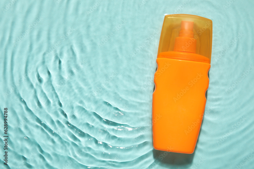 Bottle of sunscreen cream in water on color background