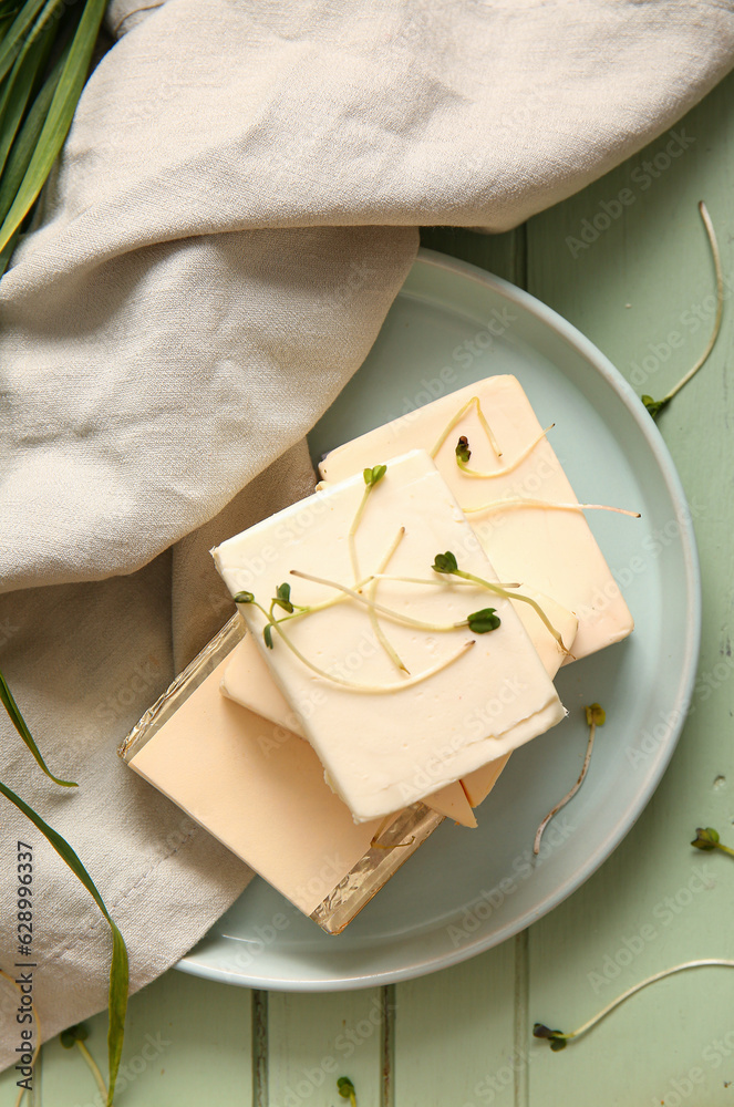 Plate with processed cheese and herbs on green wooden background