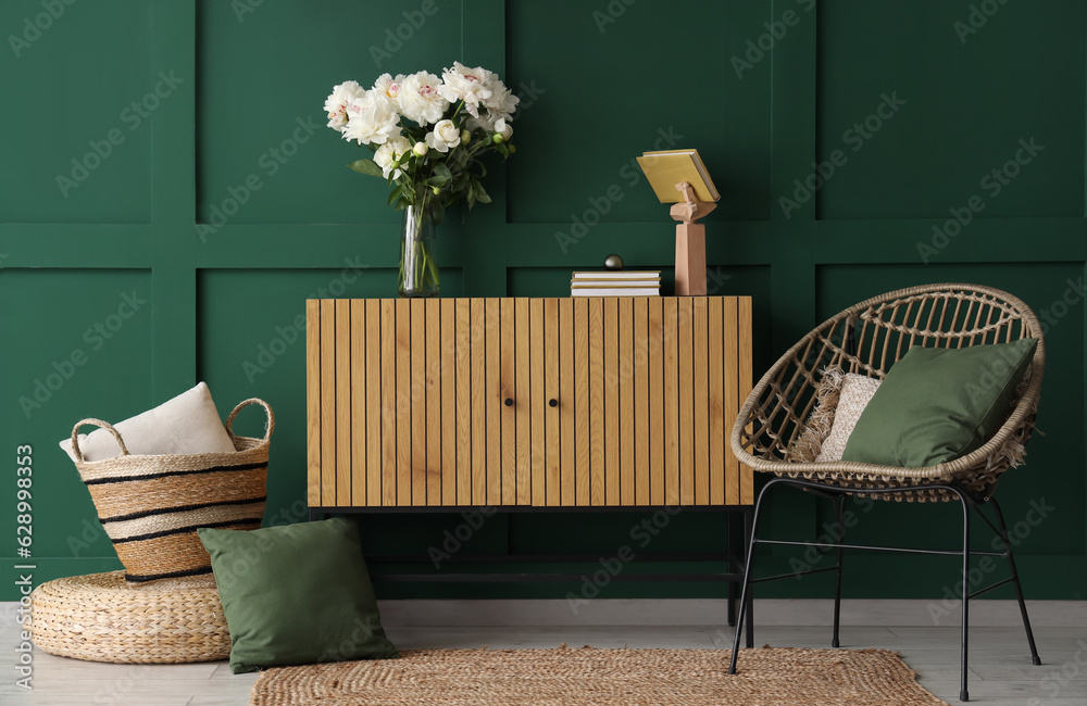 Vase of white peonies with dresser, chair and basket near green wall