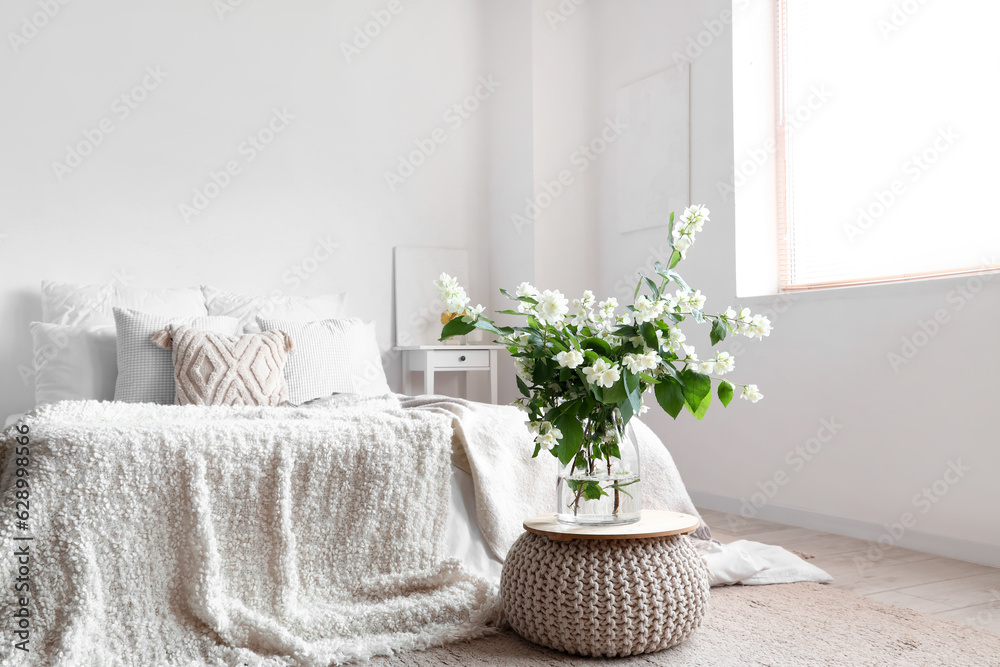 Vase with blooming jasmine flowers on pouf in interior of light bedroom