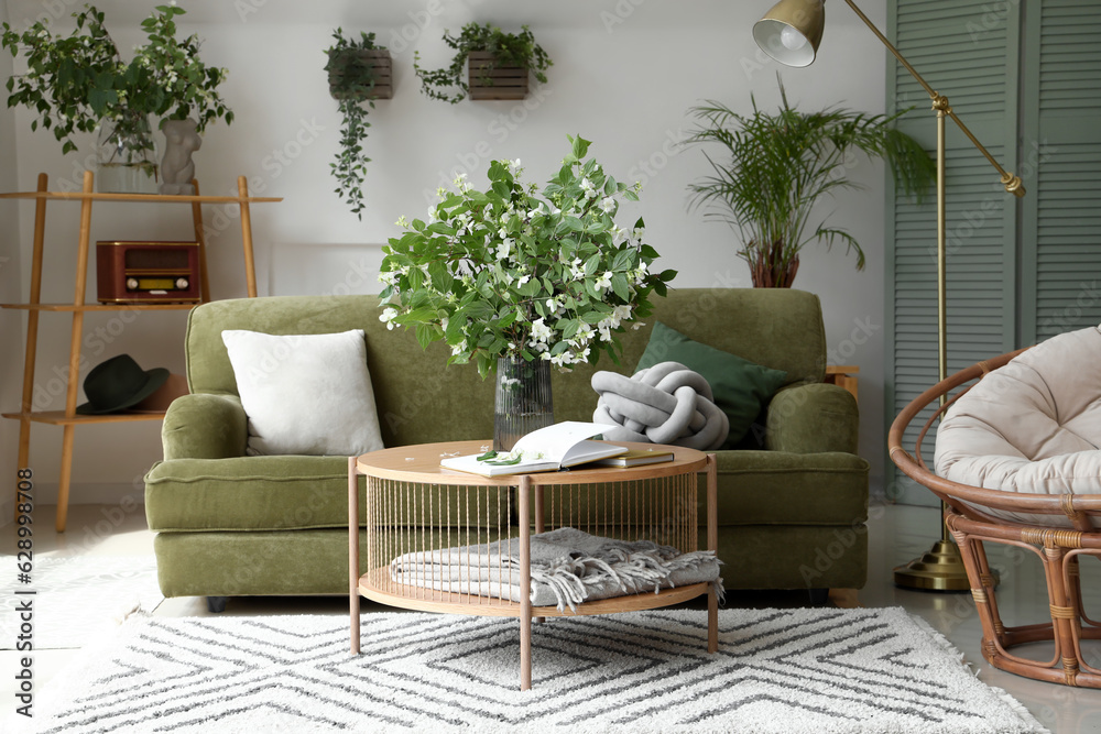 Interior of light living room with green sofa and blooming jasmine flowers on coffee table