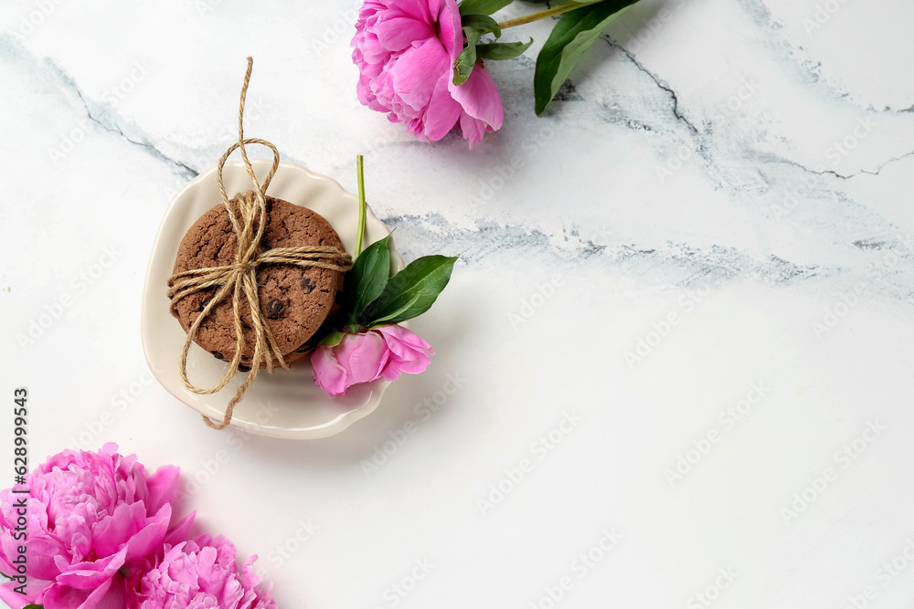 Plate with sweet cookies and beautiful peony flowers on light background