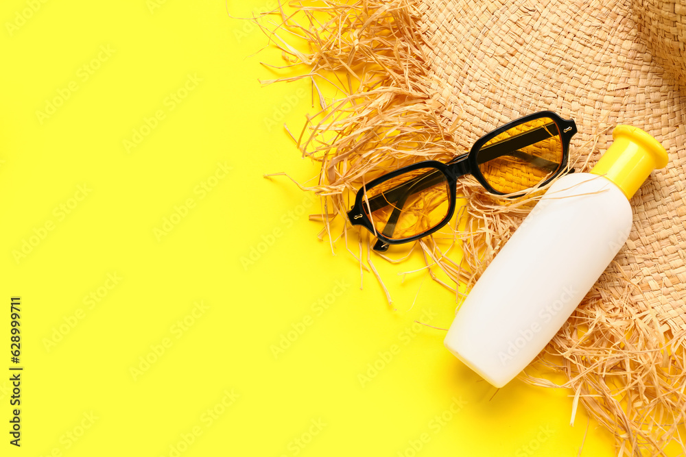 Sunglasses with bottle of sunscreen cream and wicker hat on yellow background