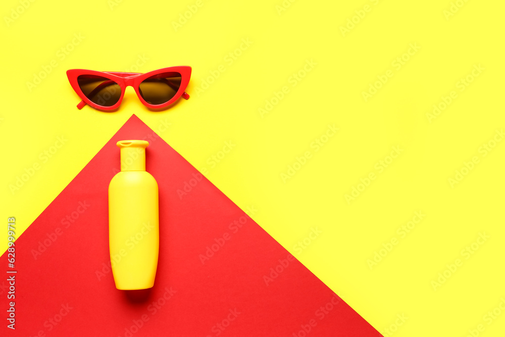 Sunglasses with bottle of sunscreen cream on color background