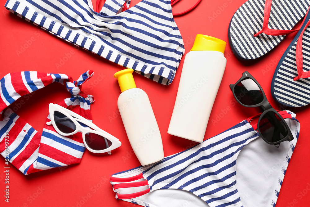 Sunglasses with swimsuit, flip flops and bottles of sunscreen cream on red background