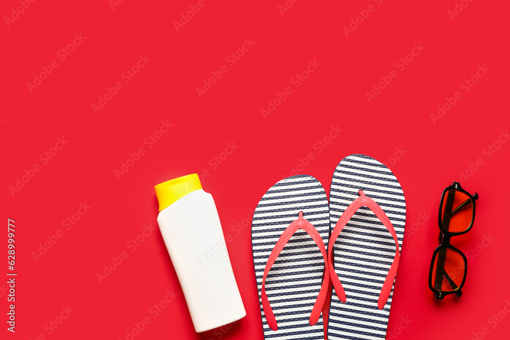 Sunglasses with flip flops and bottle of sunscreen cream on red background