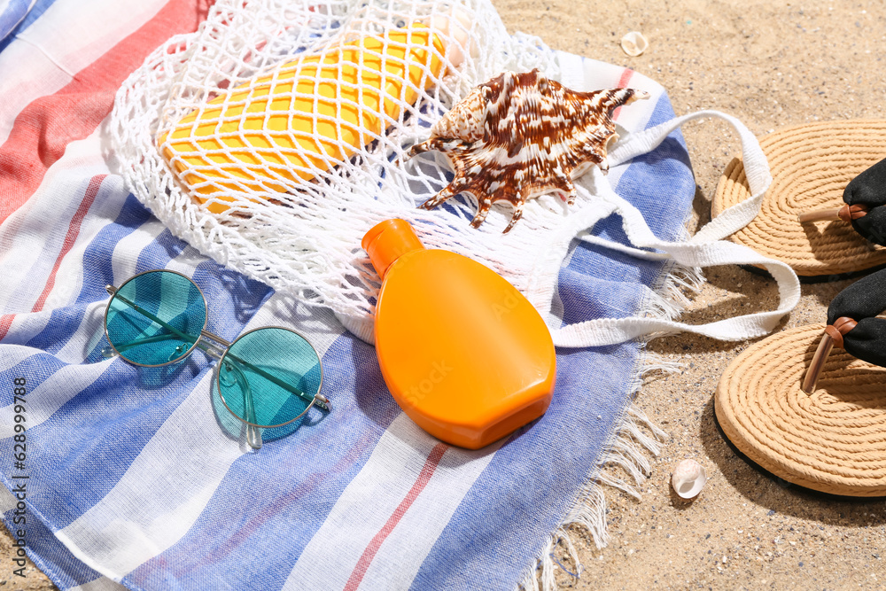 String bag with sunglasses, flip flops and bottles of sunscreen cream on sand