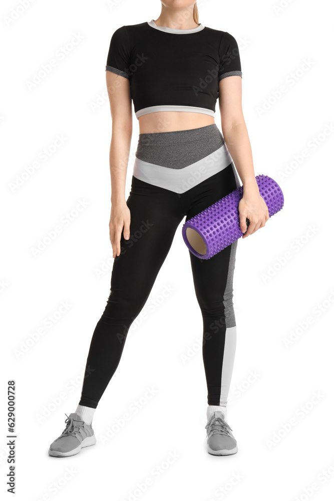 Young woman in sportswear and with foam roller on white background