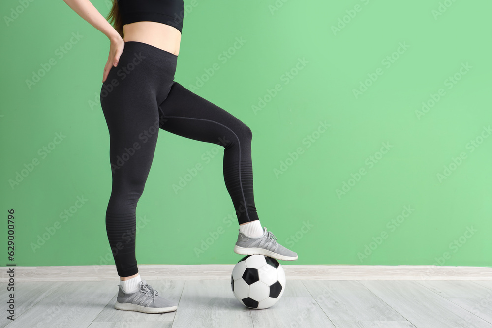 Young woman in sportswear and with soccer ball near green wall