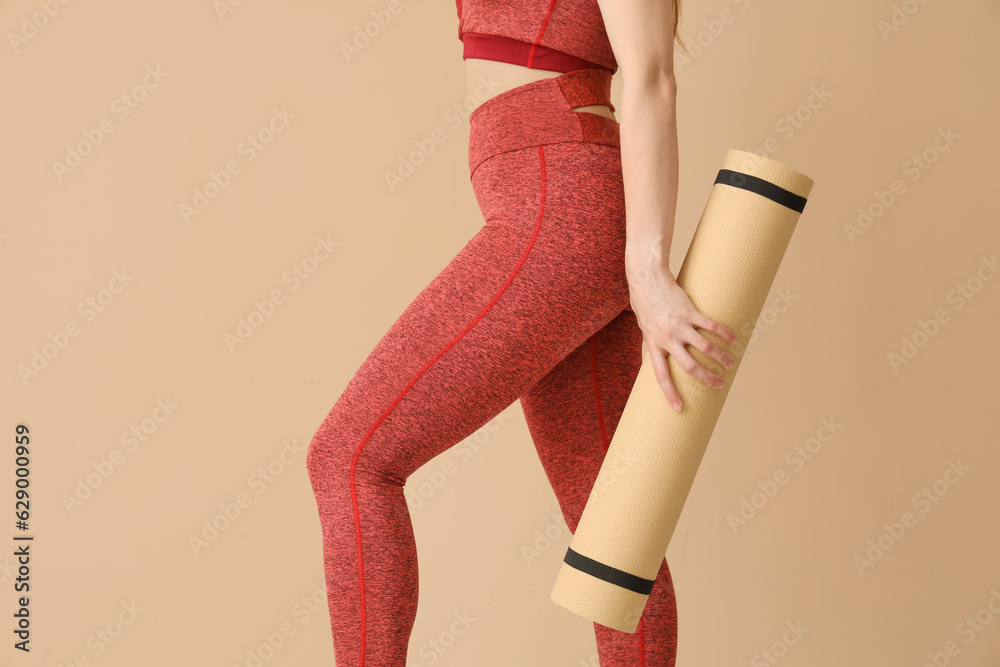 Young woman in sportswear and with yoga mat on beige background