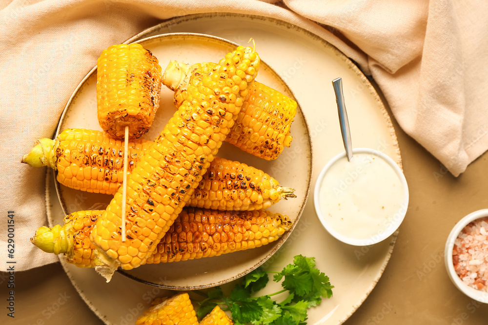 Plate with tasty grilled corn cobs and sauce on brown background