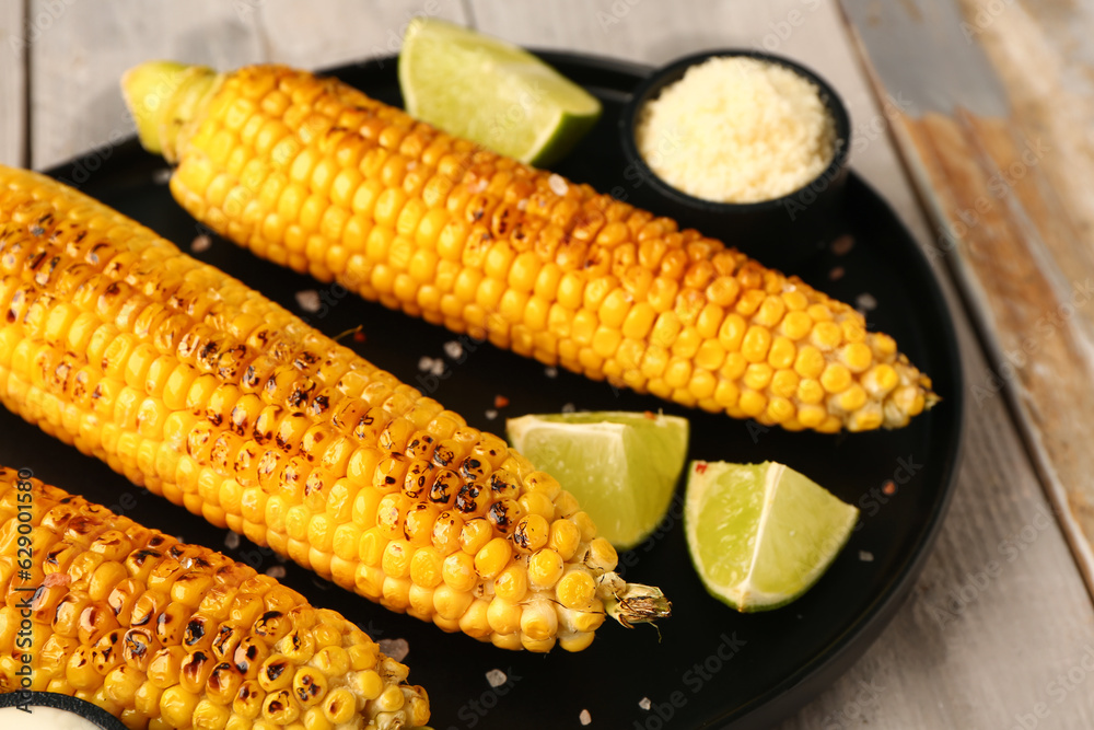 Tray with tasty grilled corn cobs and lime on grey wooden background