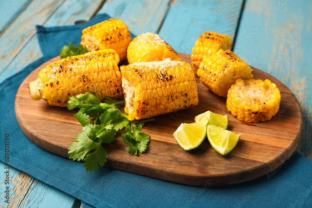 Board with cut tasty grilled corn cobs and parsley on blue wooden background