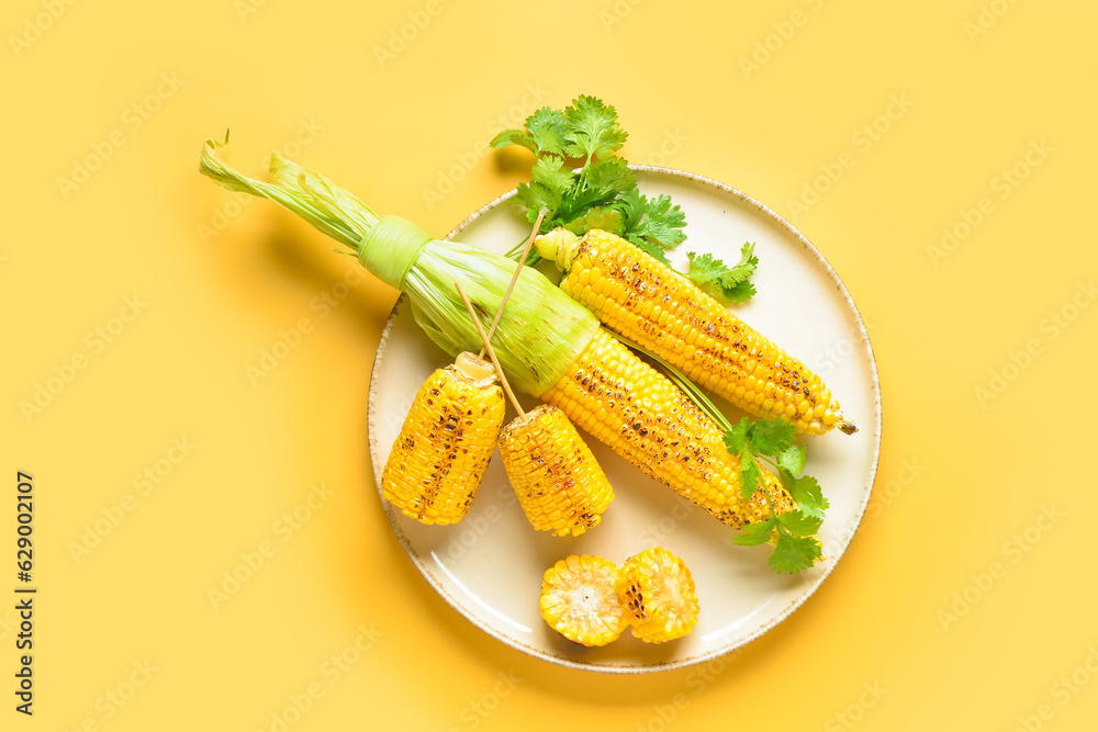 Plate with tasty grilled corn cobs and parsley on yellow background