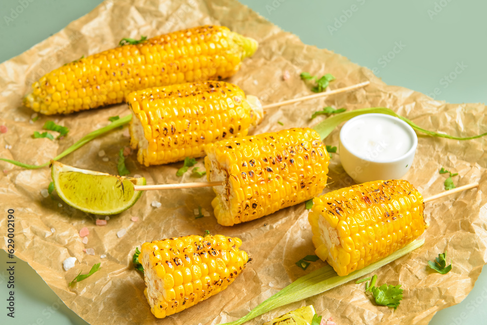 Baking paper with tasty grilled corn cob skewers and sauce on green background, closeup