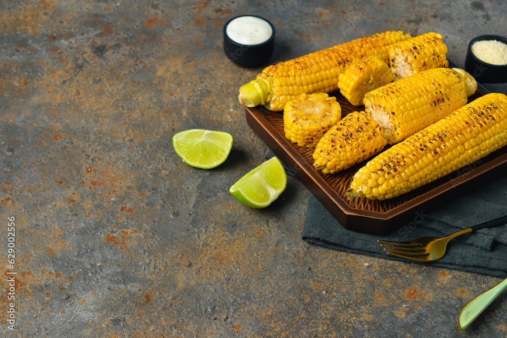 Tray with tasty grilled corn cobs and lime on dark background