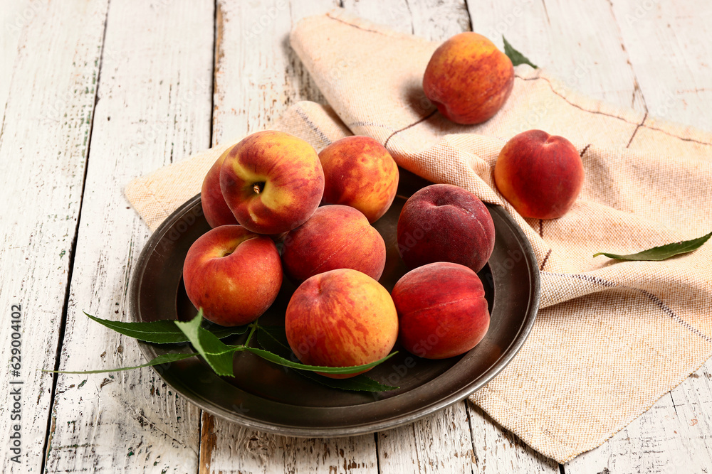 Plate with sweet peaches and leaves on white wooden background