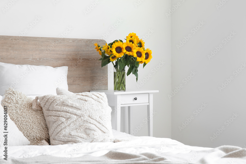 Interior of light bedroom with bouquet of sunflowers on bedside table