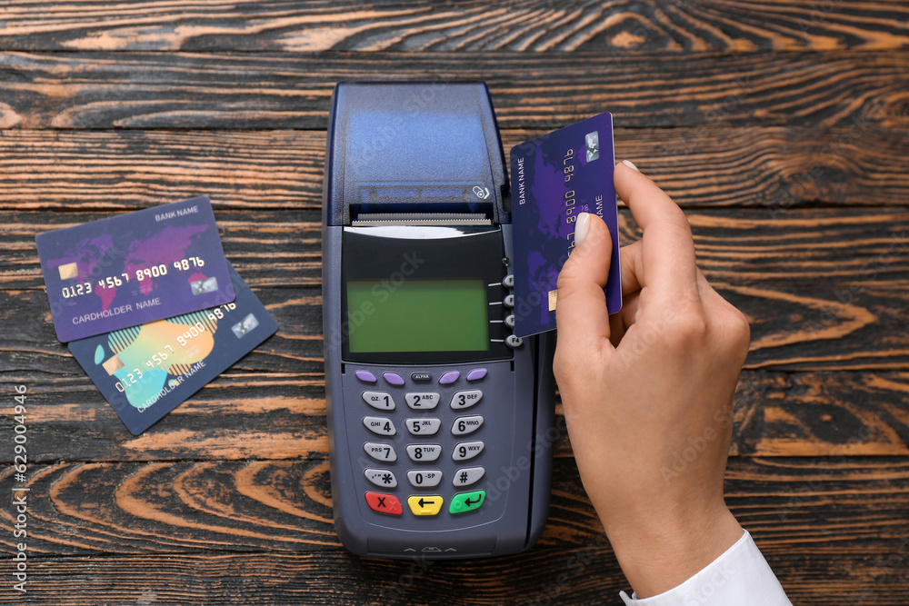 Female hand with payment terminal and credit cards on brown wooden background