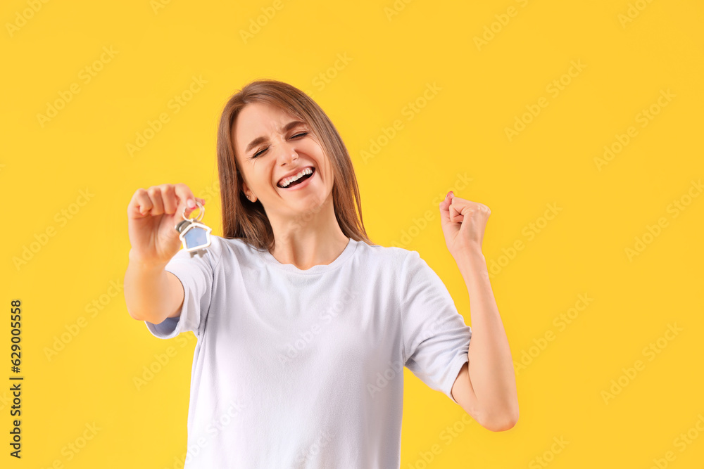 Happy young woman with keys from house on yellow background