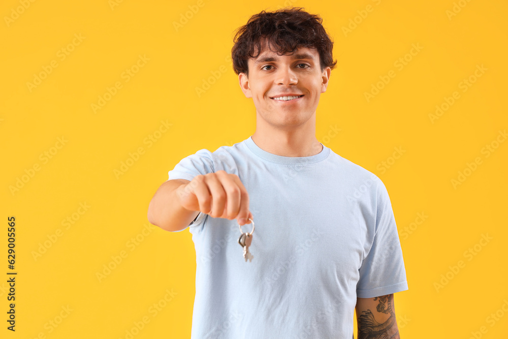 Young man with keys from house on yellow background