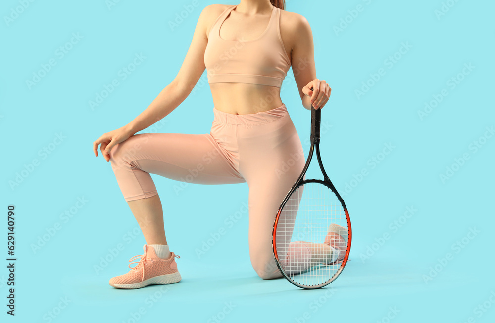 Young woman in sportswear and with tennis racket on light blue background