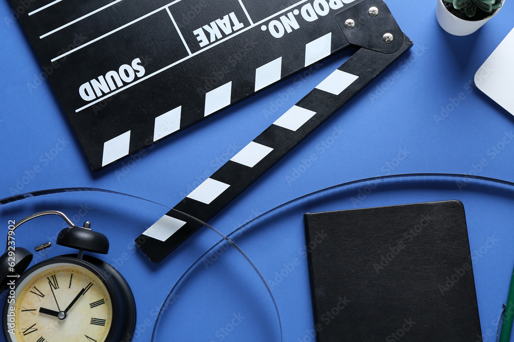 Notebook with movie clapper, film reel and alarm clock on blue background