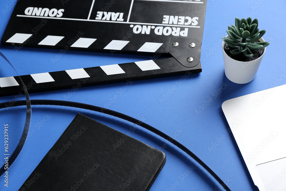 Notebook with film and movie clapper on blue background, closeup