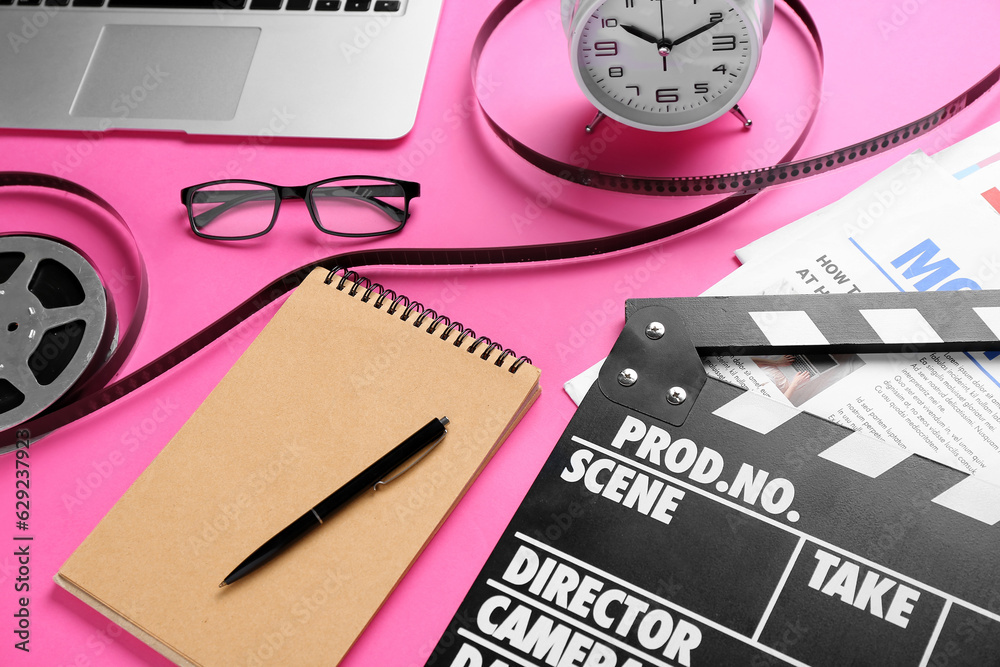 Notebook with movie clapper, film reel and alarm clock on pink background