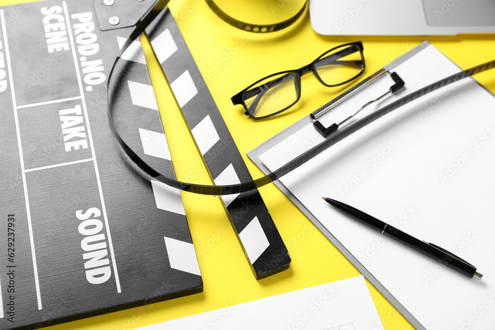 Clipboard with movie clapper and eyeglasses on yellow background, closeup