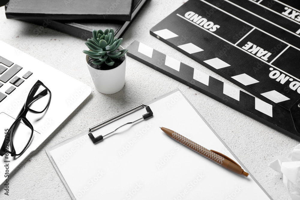 Clipboard with movie clapper, plant, eyeglasses and laptop on white background