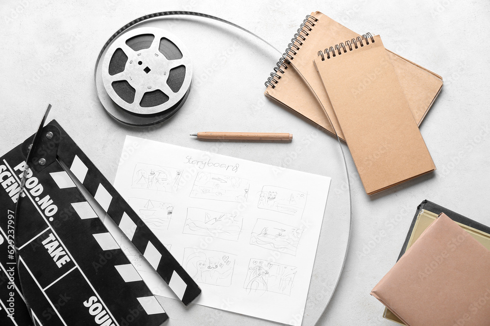 Movie clapper with storyboard, notebooks and film reel on light background