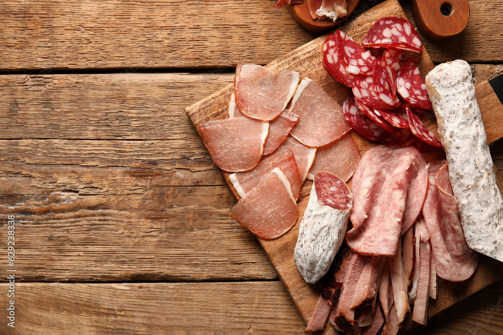 Board with assortment of tasty deli meats on wooden background