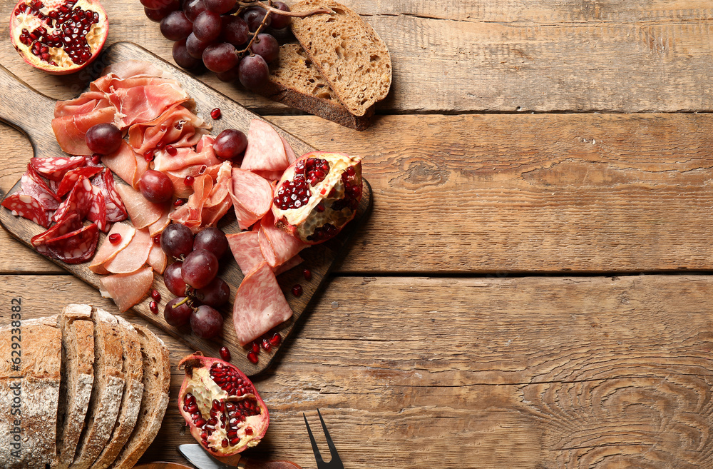 Board with assortment of tasty deli meats and bread on wooden background