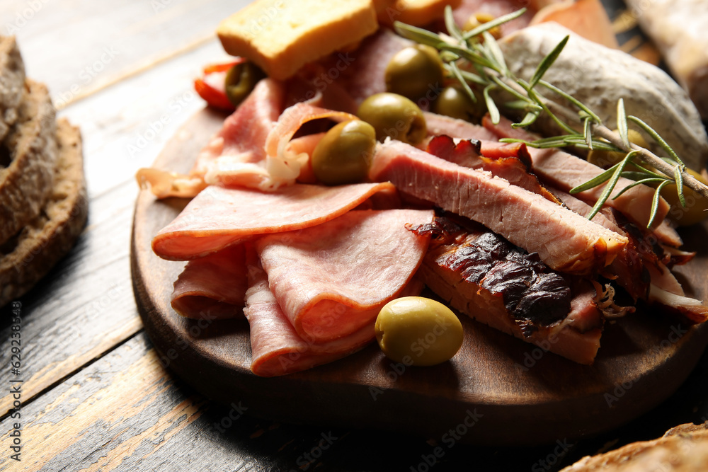 Board with assortment of tasty deli meats on table, closeup