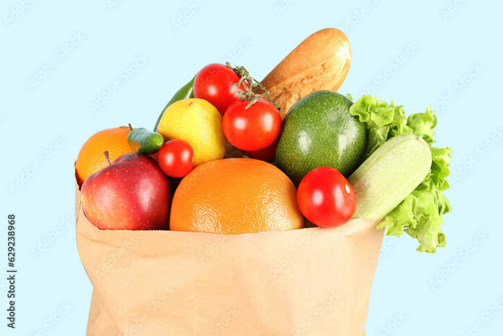 Paper bag with vegetables and fruits on light blue background