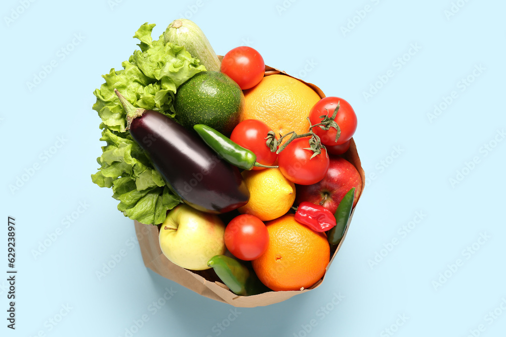 Paper bag with vegetables and fruits on light blue background