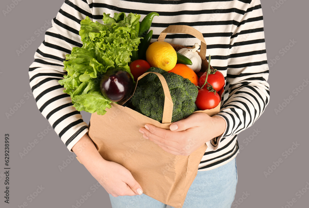 Woman holding paper bag with vegetables and fruits on grey background