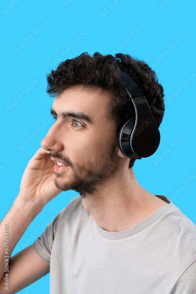 Young brunette man in headphones on blue background, closeup