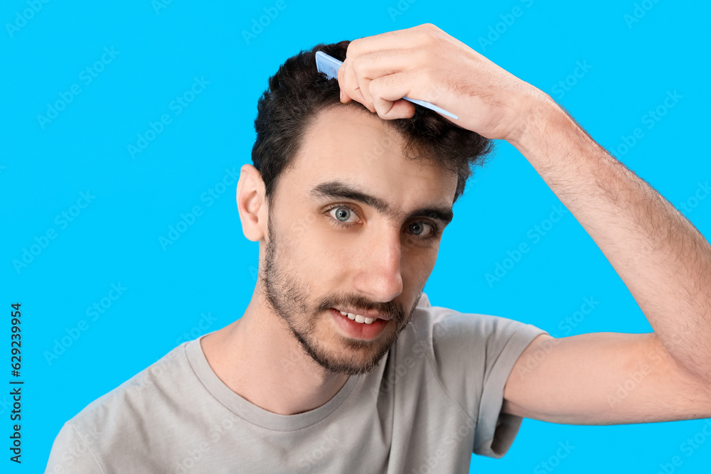 Young brunette man combing hair on blue background, closeup