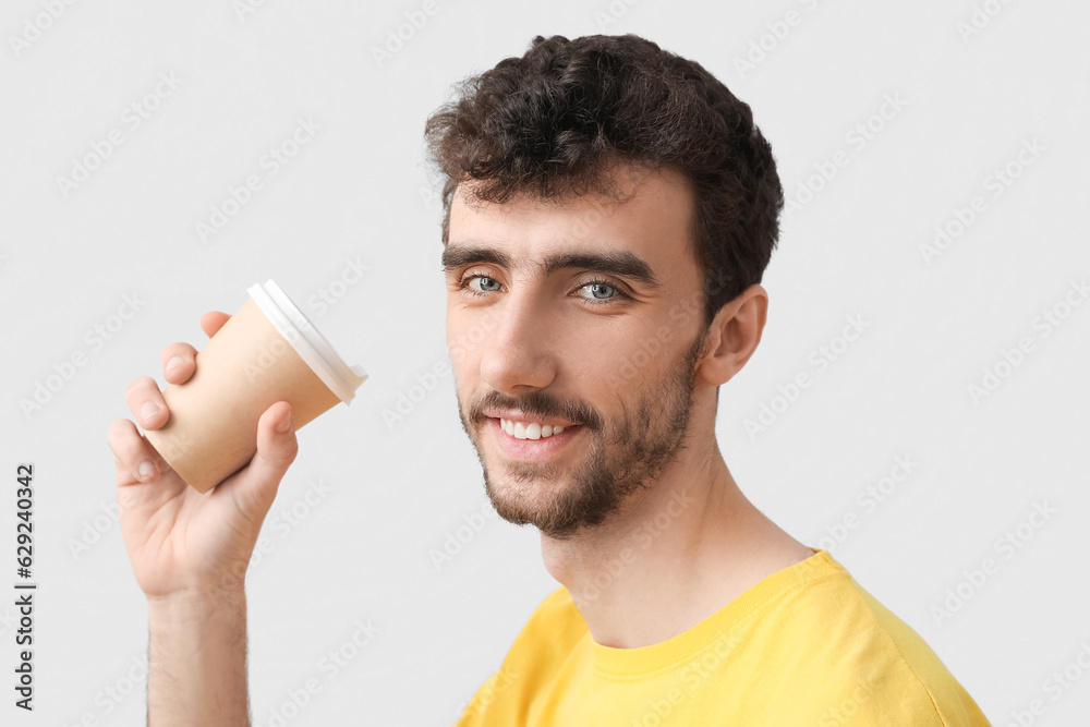 Young brunette man with cup of coffee on light background, closeup