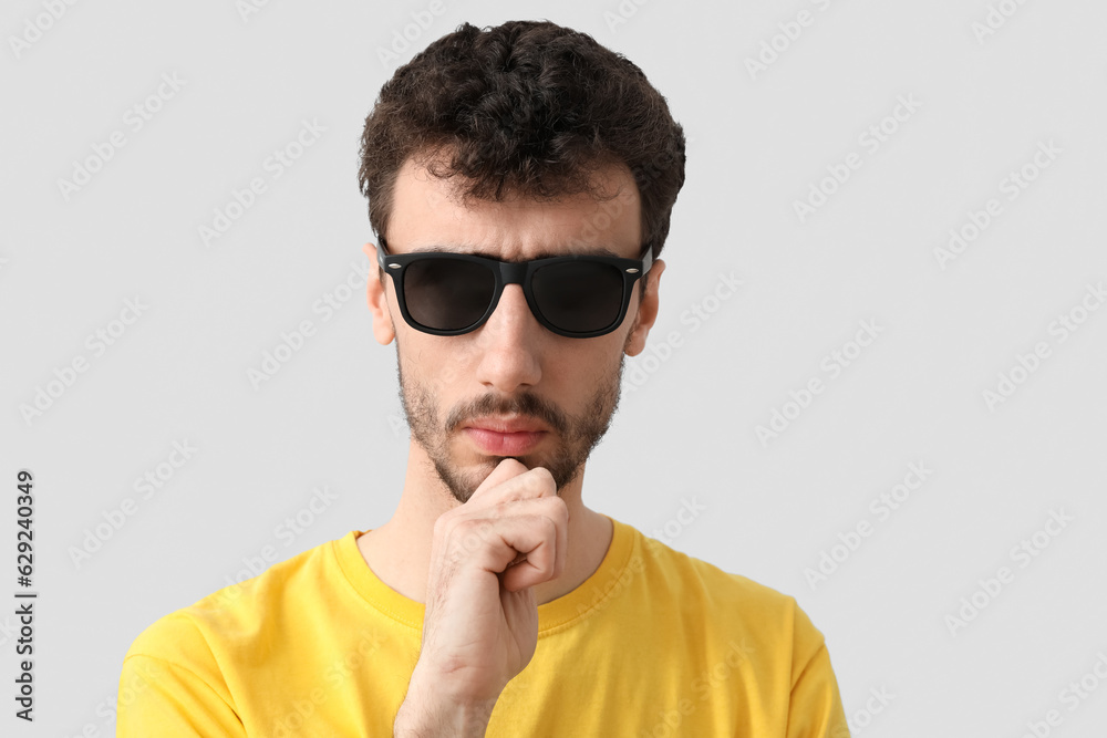 Young brunette man in sunglasses on light background, closeup