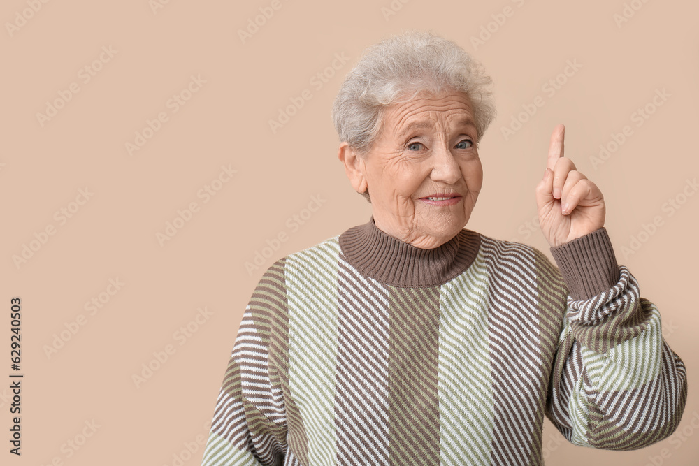 Senior woman pointing at something on beige background