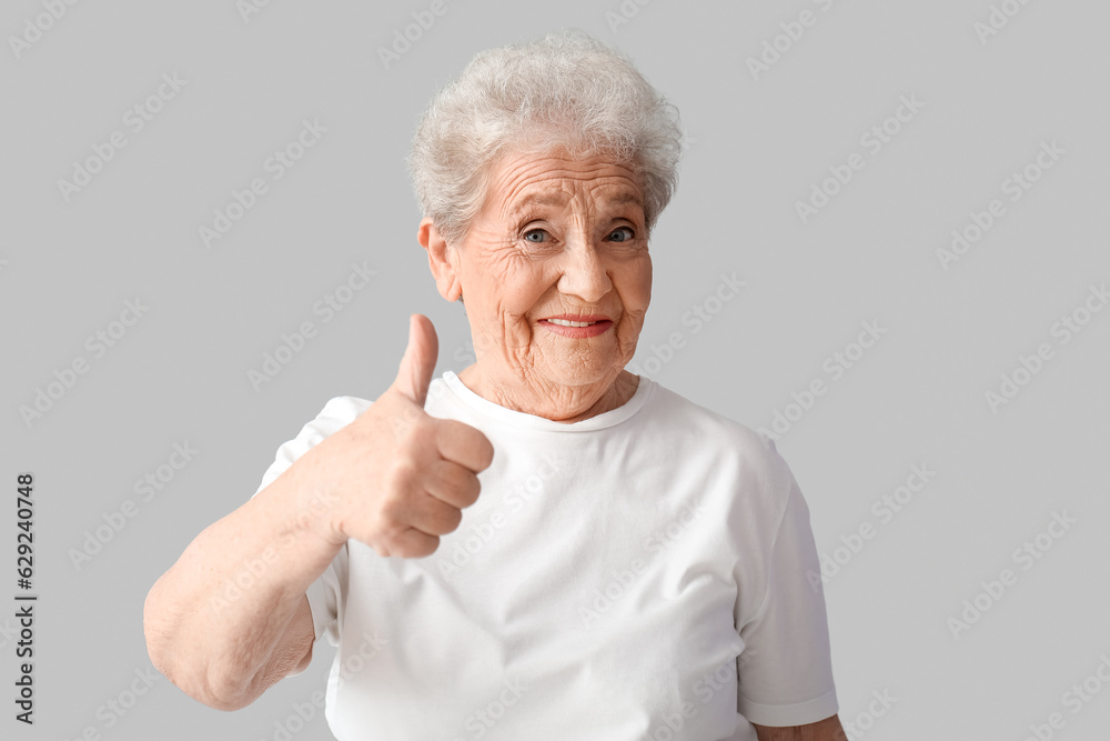 Senior woman showing thumb-up on grey background