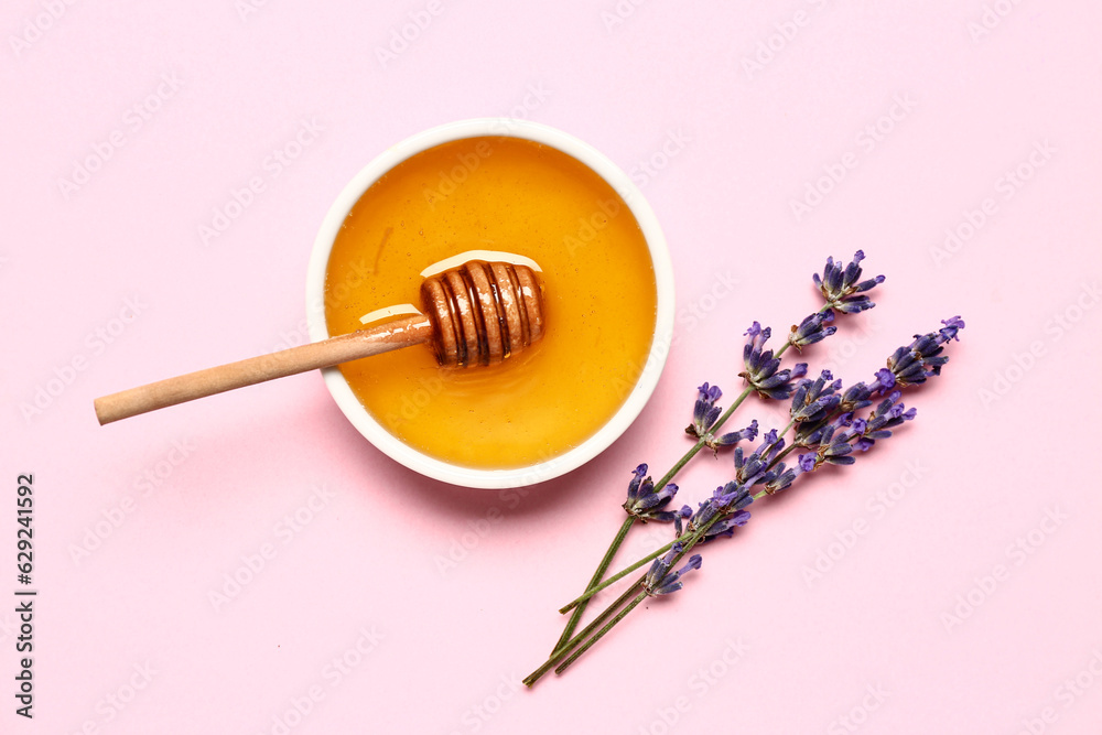 Bowl of sweet lavender honey, dipper and flowers on pink background