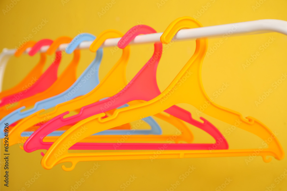 Rack with plastic clothes hangers on yellow background