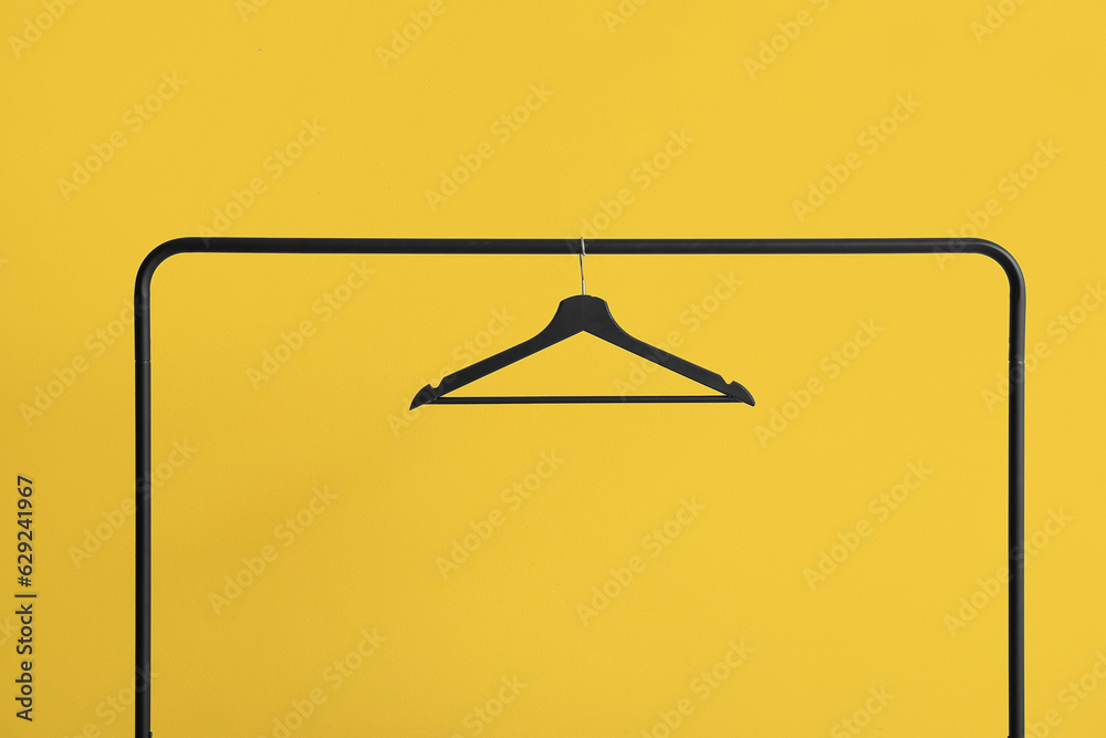 Rack with wooden clothes hanger on yellow background